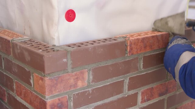 Bricklaying with precision. Builder aligning bricks carefully on wall surface. Detailed view of bricklayer securing brown bricks with precision and proper tools