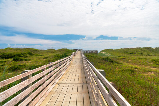 A wooden boardwalk crosses coastal dunes toward the beach in North Carolina.