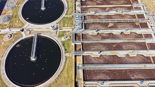 View of a wastewater treatment plant featuring large circular and rectangular tanks. Equipment is visible for the treatment process. The area is organized and industrial.