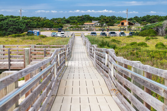 A wooden boardwalk leads from coastal dunes toward a North Carolina parking area.