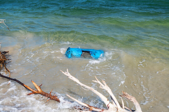 Coastal pollution from a discarded blue barrel among driftwood along the Atlantic shoreline.