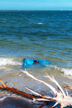 Coastal pollution in a vertical view of a discarded barrel behind driftwood.