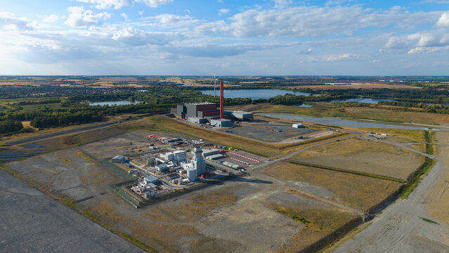 Aerial view of Millbrook Power Plant, featuring industrial infrastructure, storage tanks, and a tall chimney set within a landscape of open fields and lakes in Stewartby, England, United Kingdom.