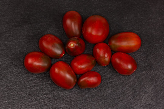 Whole small purple-brown tomatoes on black flate slate plate