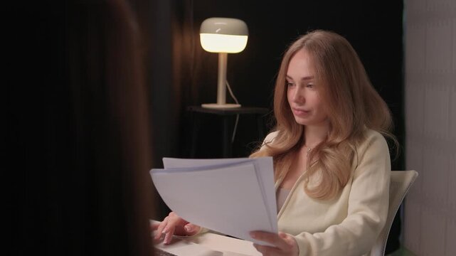 Woman recruiter gestures rejection while reviewing resumes. Caucasian female recruiter indicates rejection through hand gesture while examining applicant documents at her desk