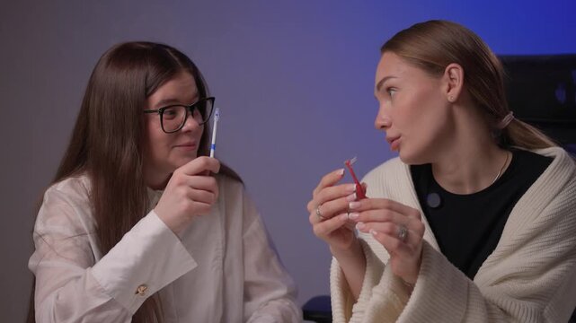 Caucasian women demonstrating brushing methods. Two women explain oral hygiene in studio setting. Women showcase proper tooth brushing techniques with educational intent