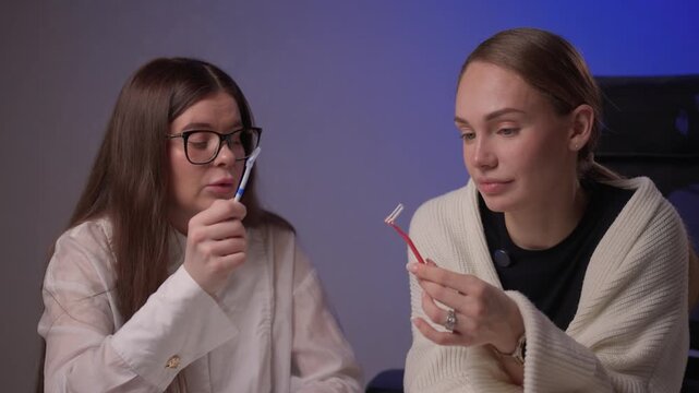 Caucasian women demonstrating brushing methods. Two women explain oral hygiene in studio setting. Women showcase proper tooth brushing techniques with educational intent