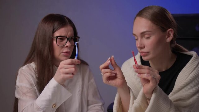 Caucasian women demonstrating brushing methods. Two women explain oral hygiene in studio setting. Women showcase proper tooth brushing techniques with educational intent