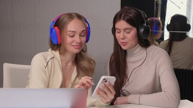 Shared phone sparks joyful interaction. Two friends enjoy viral video in cozy setting. Pair of young women engage with popular video content in comfortable creative space