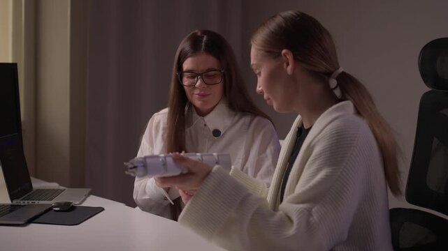Caucasian women assess smart socket functionality carefully. Two ladies of Caucasian descent collaboratively inspect and compare smart socket models on studio desk