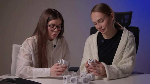 Caucasian women assess smart socket functionality carefully. Two ladies of Caucasian descent collaboratively inspect and compare smart socket models on studio desk
