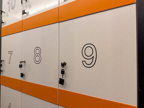 Numbered self service storage lockers with keys, white and orange secure compartments for luggage and personal belongings in a modern public facility.