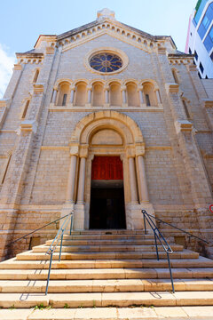 Facade of a Romanesque-style stone church with rose window, arched portal in Cannes, French Riviera, Cote d'Azur, France