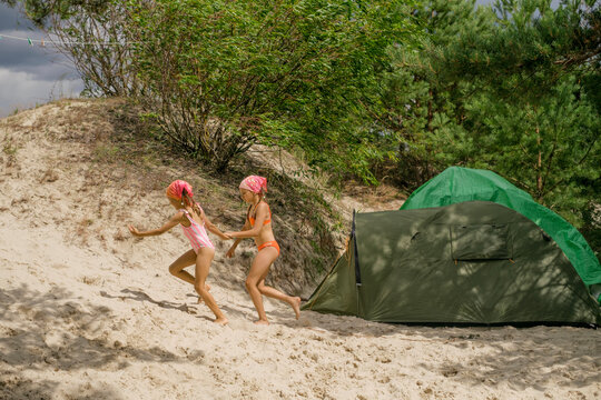 Girls in swimsuits, having fun together, are running along the beach by the lake. A children&rsquo;s camping camp.