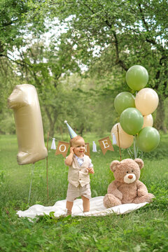 A child in a party hat with balloons shaped like the number one is celebrating their first birthday.