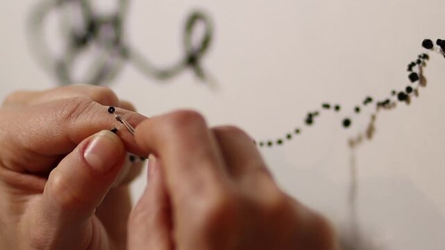 Macro shot focusing on hands holding a crochet hook and stringing black beads to create a unique decorative art piece. Detailed view of needlework and craftmanship.