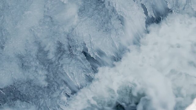 Rushing whitewater rapids churning foam over ice. Close up winter river current.