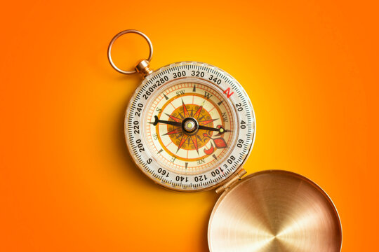 Vintage brass pocket compass open on vibrant orange background. Business navigation, strategic direction, career path guidance, decision making and outdoor exploration concept.