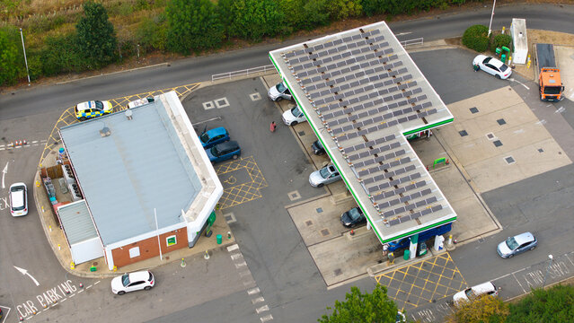Aerial view of a gas station with solar panels installed on the roof, featuring parked cars and a police vehicle in the parking lot Bedford, England, United Kingdom.