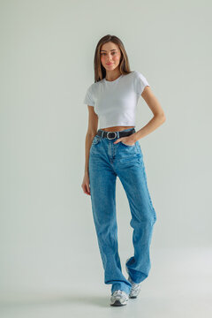 Model stands full length with hand in pocket of blue denim trousers, marketplace card built from clean frame, content for clothing shop. Wide shot. Concept of marketplace photo of whole outfit