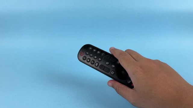 Hand Holding TV Remote Control Pointing Forward on Blue Background