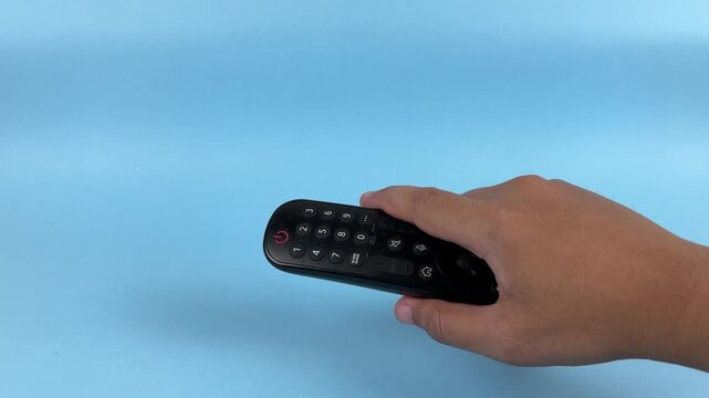 Hand Holding TV Remote Control Pointing Forward on Blue Background