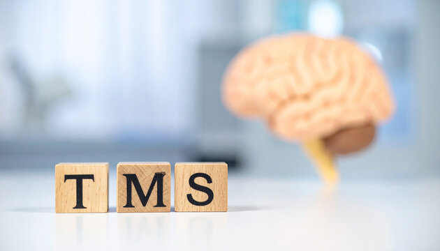 Wooden cubes spelling TMS on clinical surface, blurred anatomical brain model on background, Transcranial Magnetic Stimulation, modern medical research concept. Close-up.