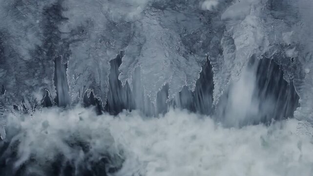 Icicles hanging above white water splash. Close up winter river cascade detail.