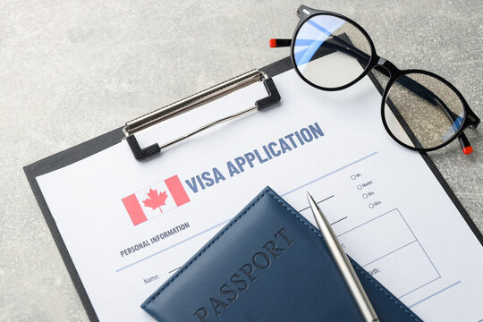 Visa application form, passport, pen and glasses on grey table, above view