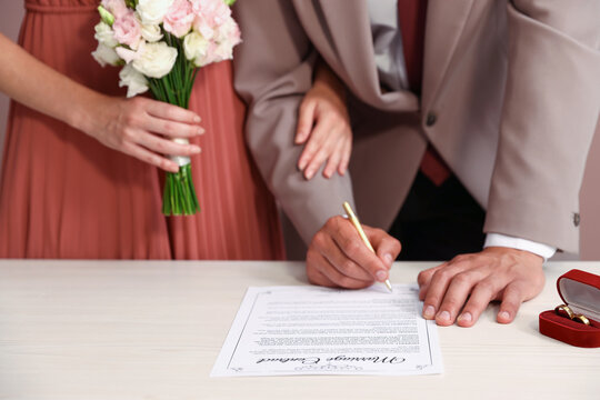 Couple signing marriage contract at white table indoors, closeup