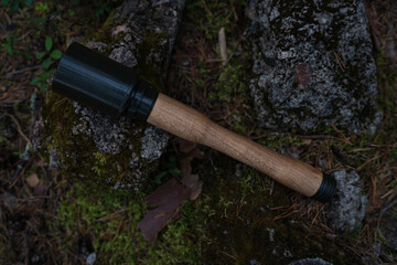Obraz premium ​Wooden and 3D printed replica of WWII German Stielhandgranate stick grenade lying on atmospheric mossy forest ground near rocks.