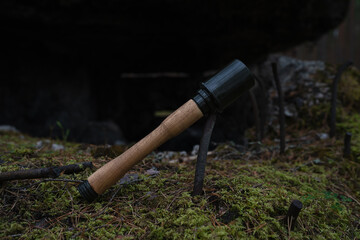 Obraz premium ​Wooden and 3D printed replica of WWII German Stielhandgranate stick grenade lying on mossy ground near a ruined old bunker.