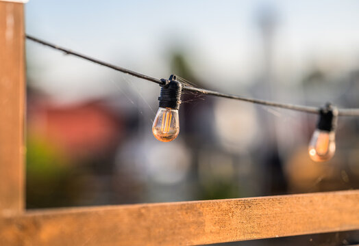 Glowing filament bulb on outdoor string light above fence.