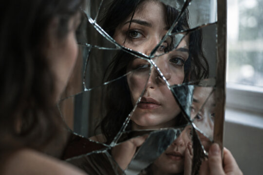Shattered mirror reflecting fragmented facial features with soft window lighting.