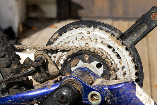 Dirty bicycle drivetrain with mud stained chain, worn crankset, chainring, sprocket, gears and pedal assembly, featuring rust marks, blue frame, metal texture and closeup repair detail