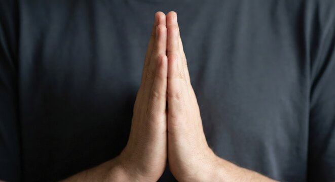 Man holding hands in prayer position or meditating gesture against dark background