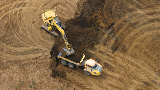 Aerial view of an excavator loading soil into a dump truck at a construction site with tire tracks in the dirt at the Black Cat Roundabout in Chawston, England, United Kingdom.