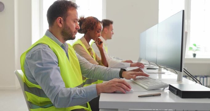 Dispatchers team monitoring logistics on office computers. Focused operators in safety vests coordinate control and tracking at modern workstations. Clear focus on efficient operations.