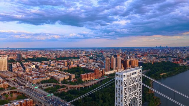 George Washington Bridge and upper Manhattan beneath clouds. A bridge tower rises above roads and apartment blocks beneath a blue and gray sky.