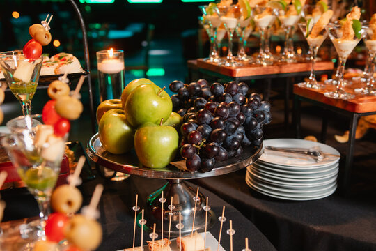 Catering table decorated with a fruit centerpiece featuring green apples, grapes, etc.