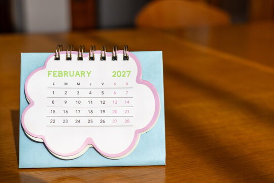 February 2027. Image of a pastel-colored desk calendar placed on a wooden desk