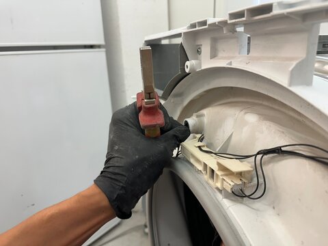 Appliance technician in black gloves using pliers to repair or disconnect internal parts of a washing machine or dryer during maintenance service, close-up shot.