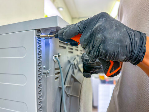 Appliance repair service technician using an electric screwdriver bit to fix the back panel of a washing machine, close-up shot.