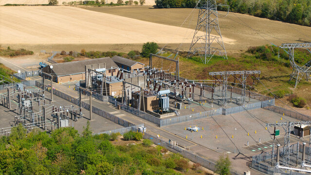 Aerial view of Eaton Socon Substation with electrical transformers, switchgear, and power lines surrounded by agricultural fields and trees in St. Neots, England, United Kingdom.