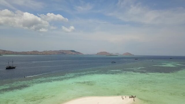 Bird's eye view of turquoise coral reef surrounding tiny white sand island in Taka Makassar