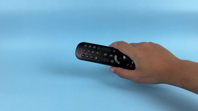 Hand Holding TV Remote Control Pointing Forward on Blue Background