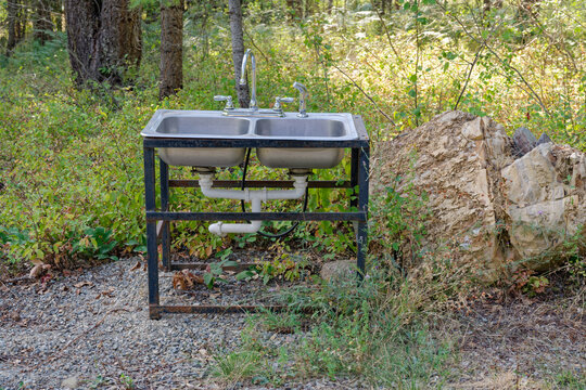 An outdoor sink in the woods with two basins, plumbed faucets and drains