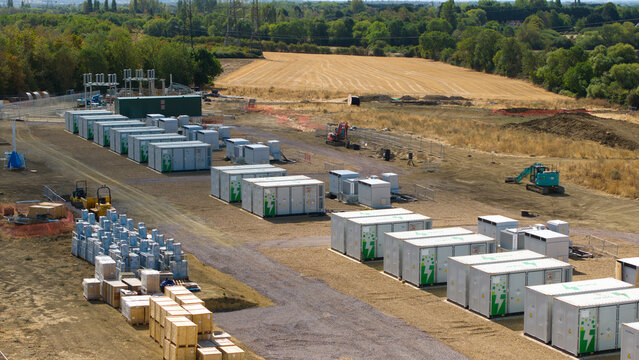Aerial view of the Eaton Socon Substation featuring rows of battery energy storage containers with green logos, construction equipment, and wooden crates in St. Neots, England, United Kingdom.