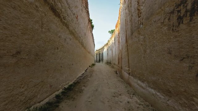 Natural limestone gully carving narrow, sunlit passage path, rugged cliffs toward the ocean at Green Bowl Beach, Bali secluded textured peaceful coastal trail for travel and exploration. Drone flight
