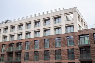 Fototapeta premium Modern apartment building shows rows of windows and balconies. Brick walls, glass railings, and rooftop equipment shape the urban facade. Residential architecture and real estate concept.